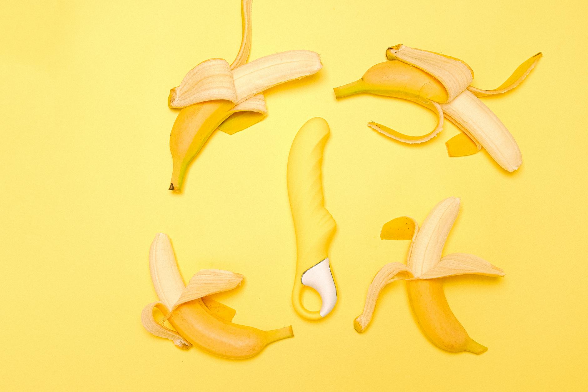 Vibrador de silicone amarelo rodeado de bananas descascadas em fundo amarelo