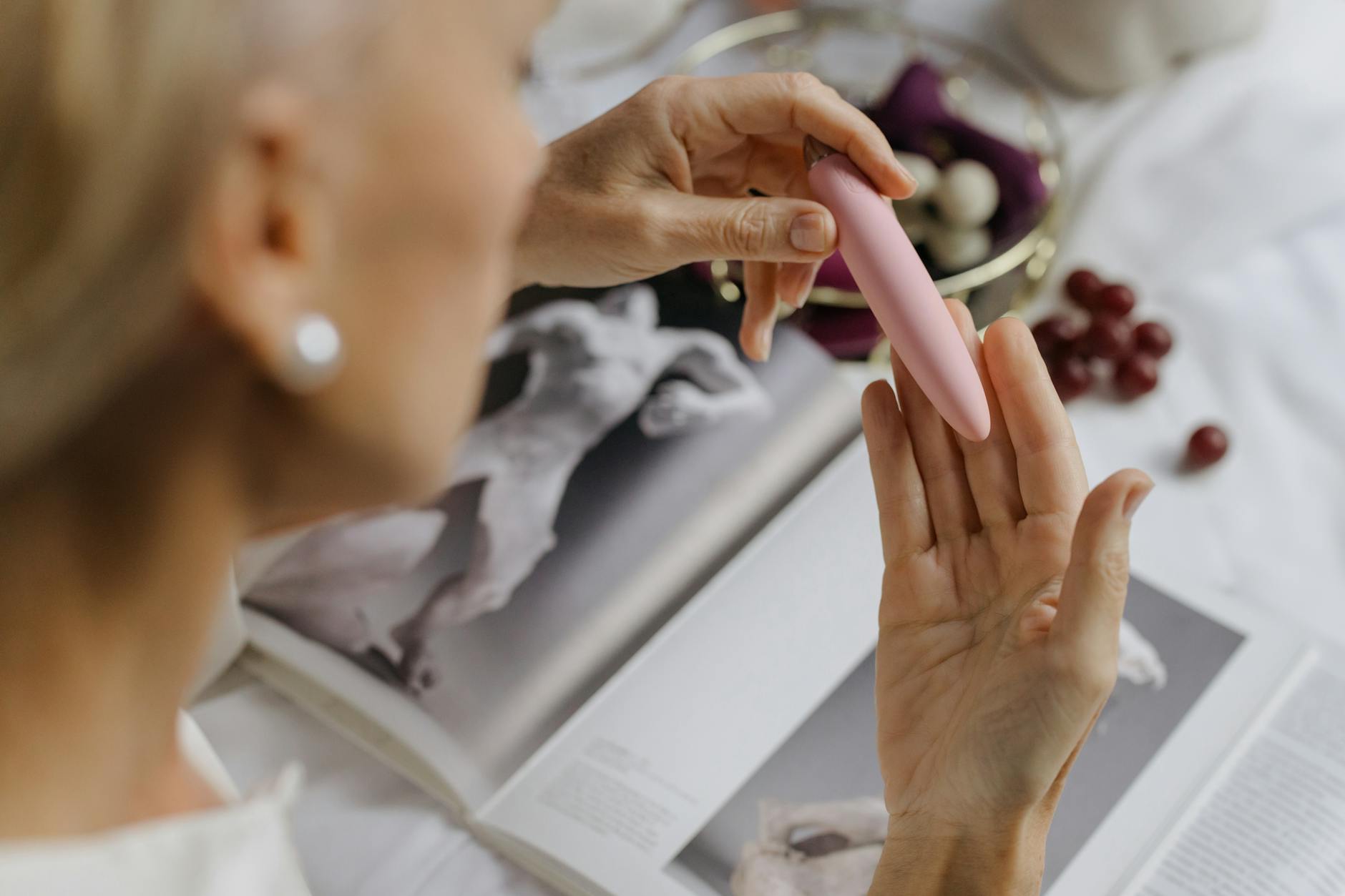 Mulher segurando um vibrador rosa, com arte e livros ao fundo, destacando intimidade pessoal