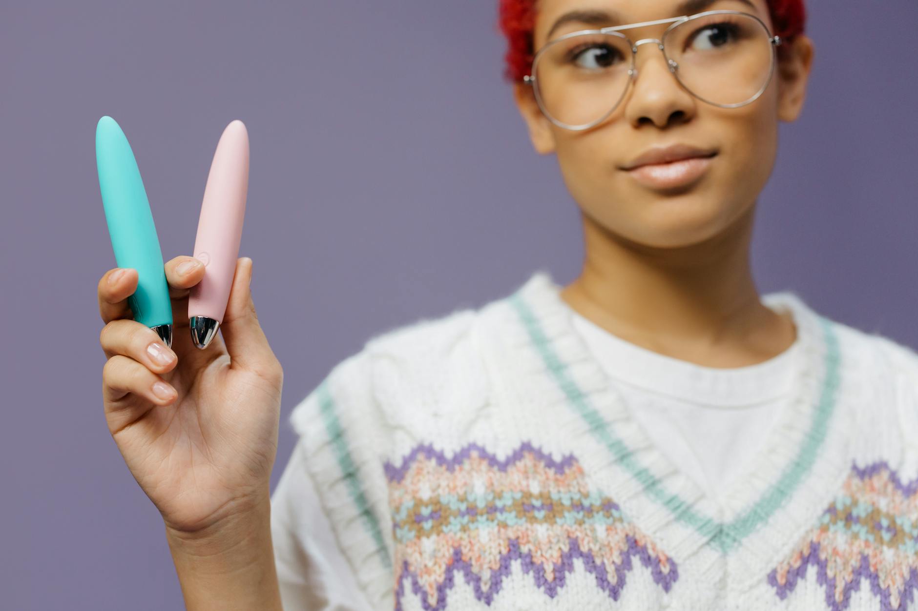 Woman holding colorful vibrators against a purple background, representing sex toy exploration and personal empowerment.