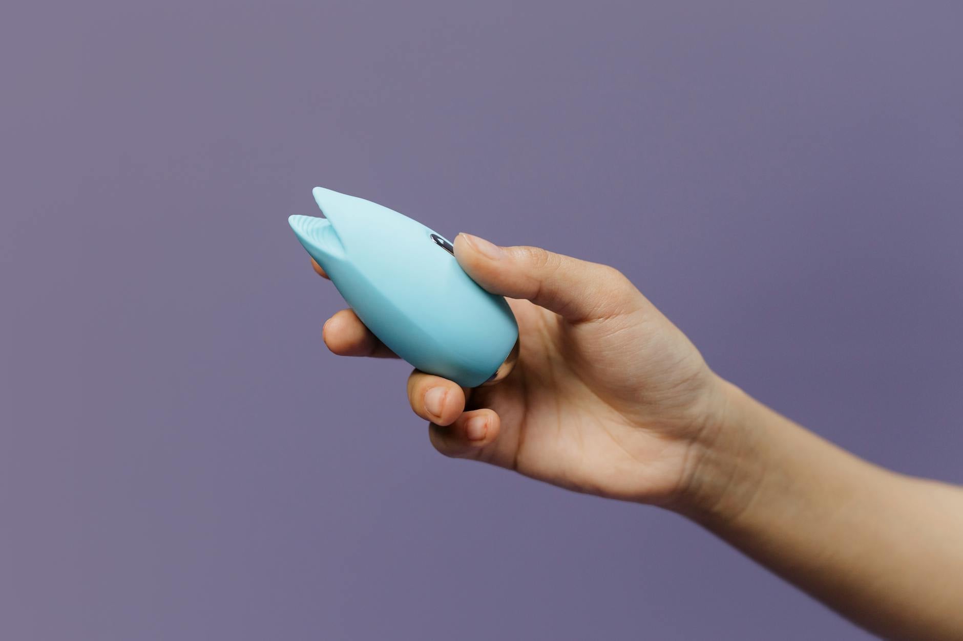 Vibrador de silicone azul em mão contra fundo roxo sólido, promovendo amor próprio e sexualidade